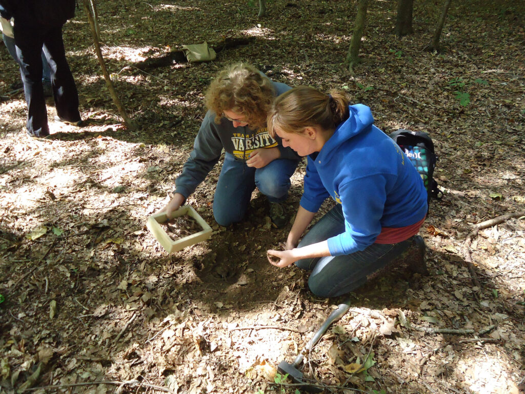 Two students in the woods sifting through dirt.