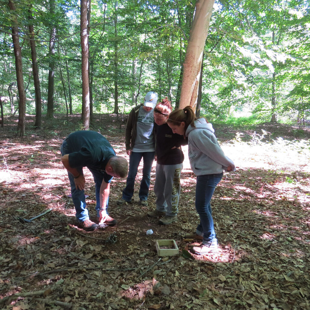 Photo of Dan and 3 students in Pennsylvania woods. Dan is showing them how to set traps.