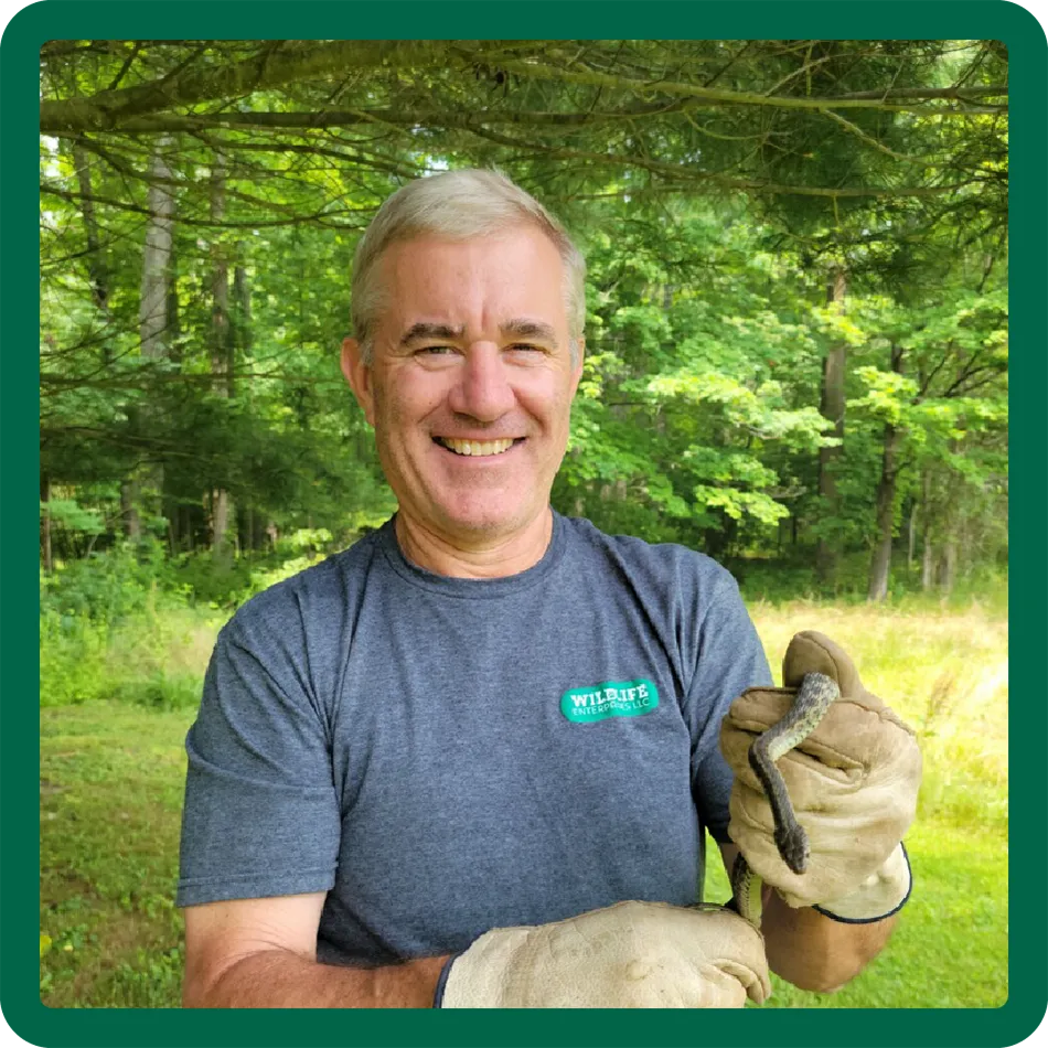 Dan Lynch holding a snake and standing in front of the woods